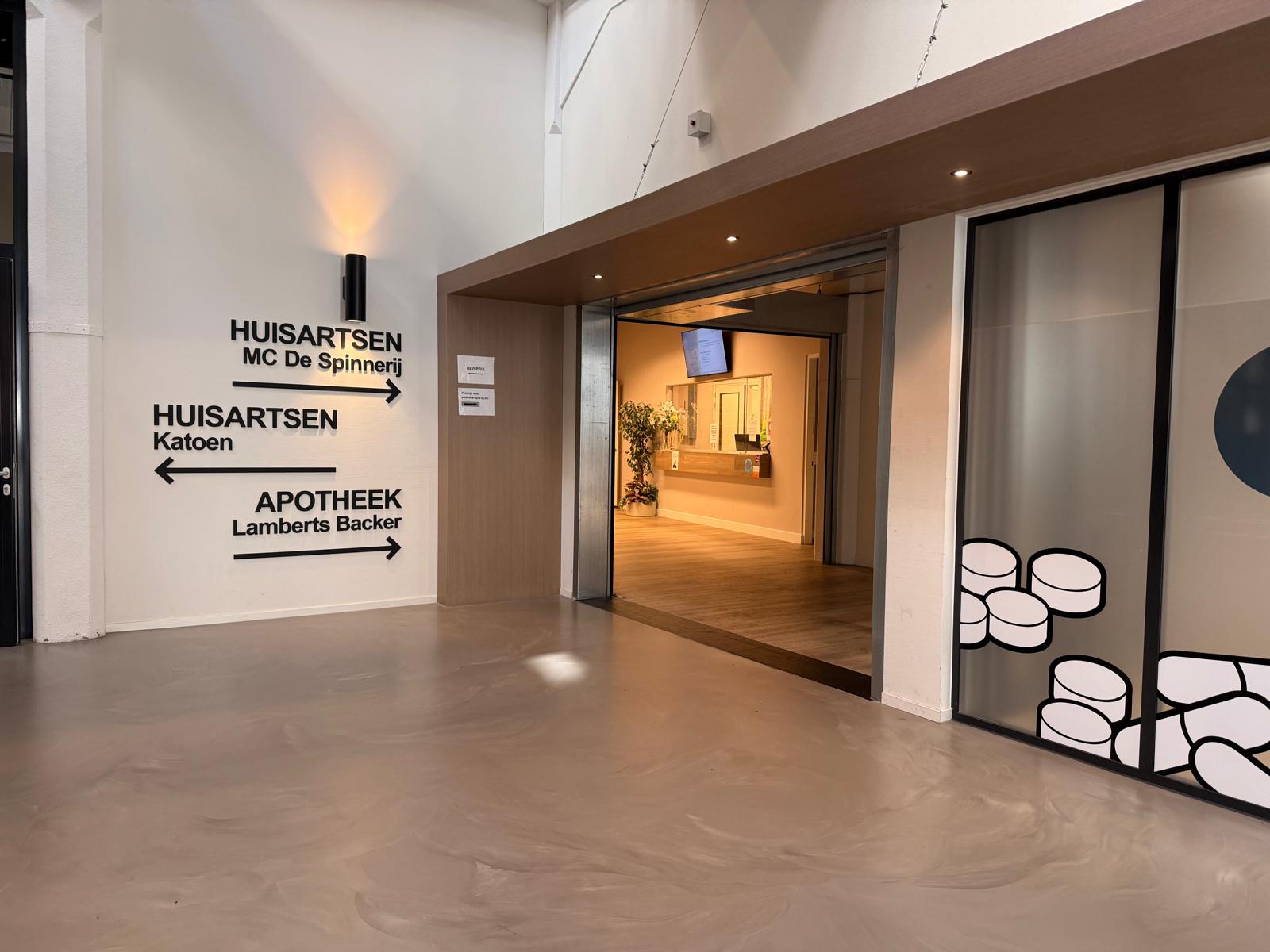 De ingang van de praktijk in het Twenthe Centrum, met de bewegwijzering naar de huisartsen en de apotheek